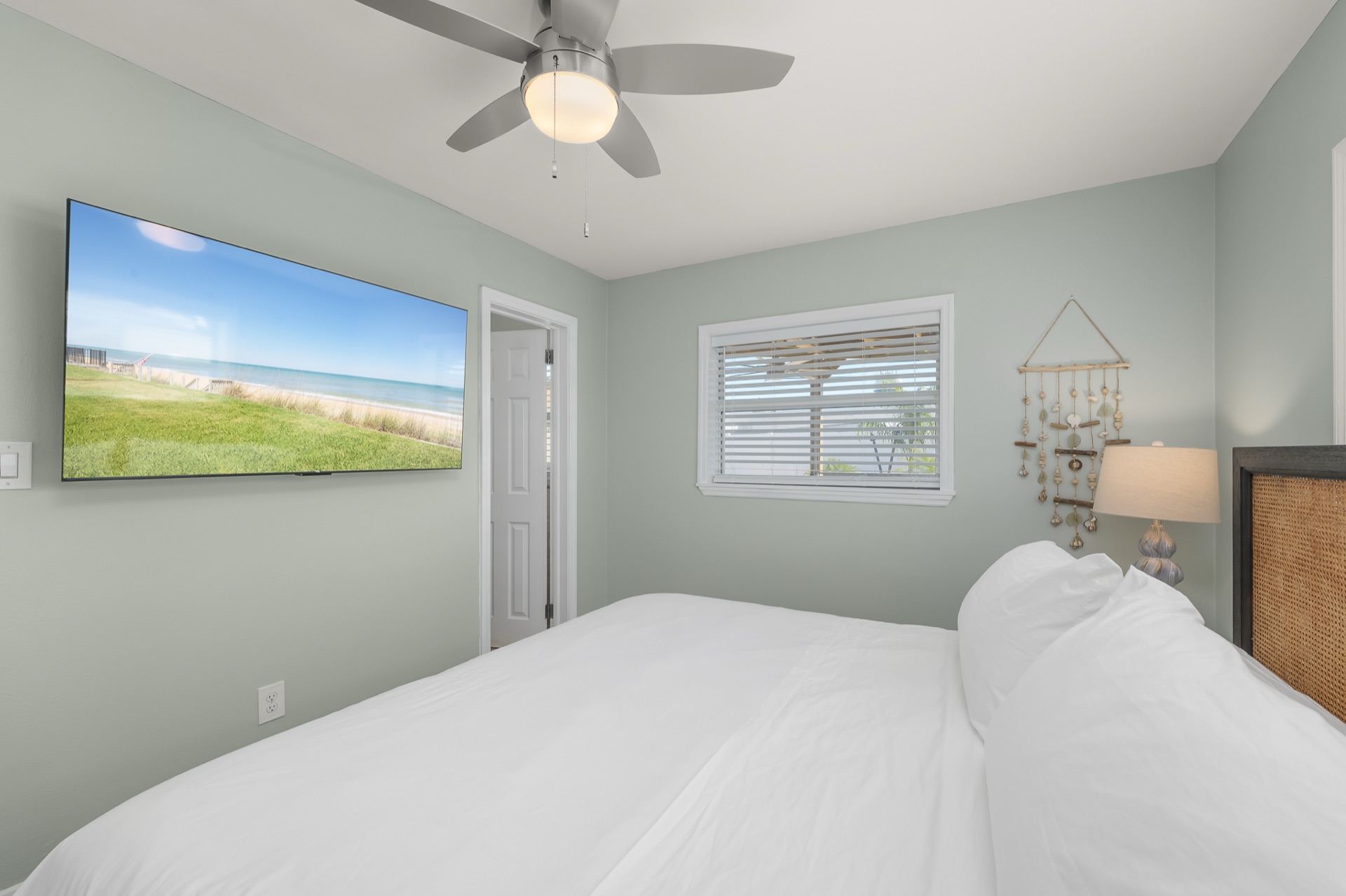 The same bedroom at Shell Yeah with a wall-mounted TV and a handmade shell wall hanging